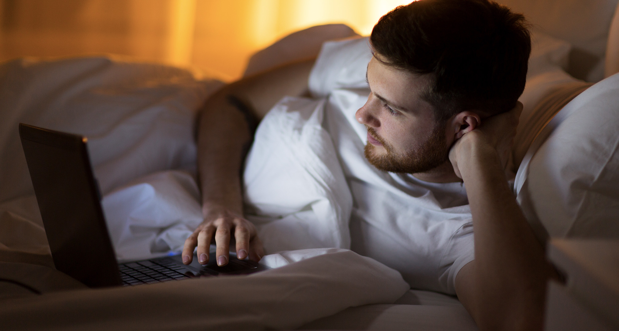 person, der bruger laptop fra sengen om natten